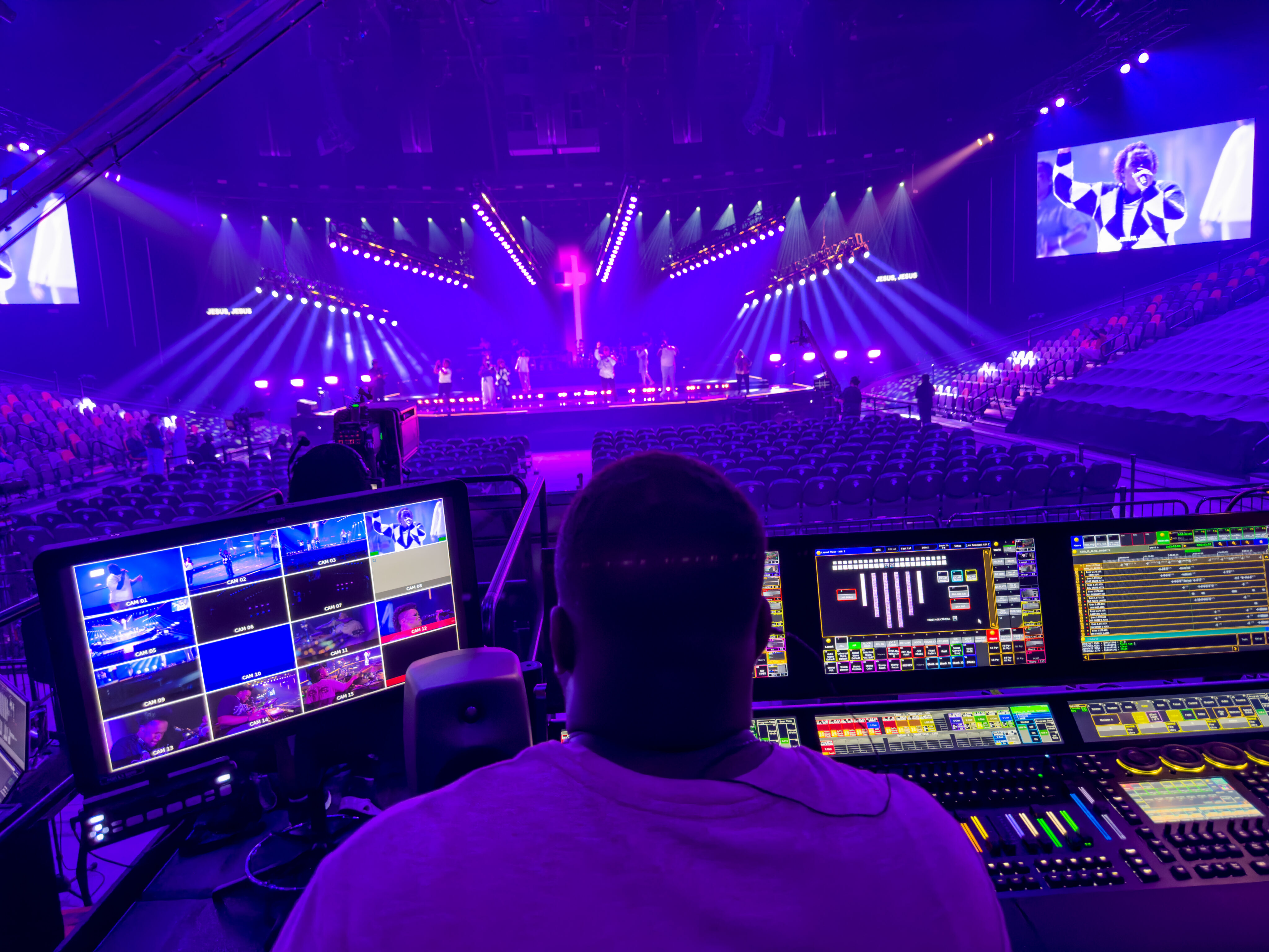 Production operator working in the Transformation Church control room with live stage feeds visible on monitors.