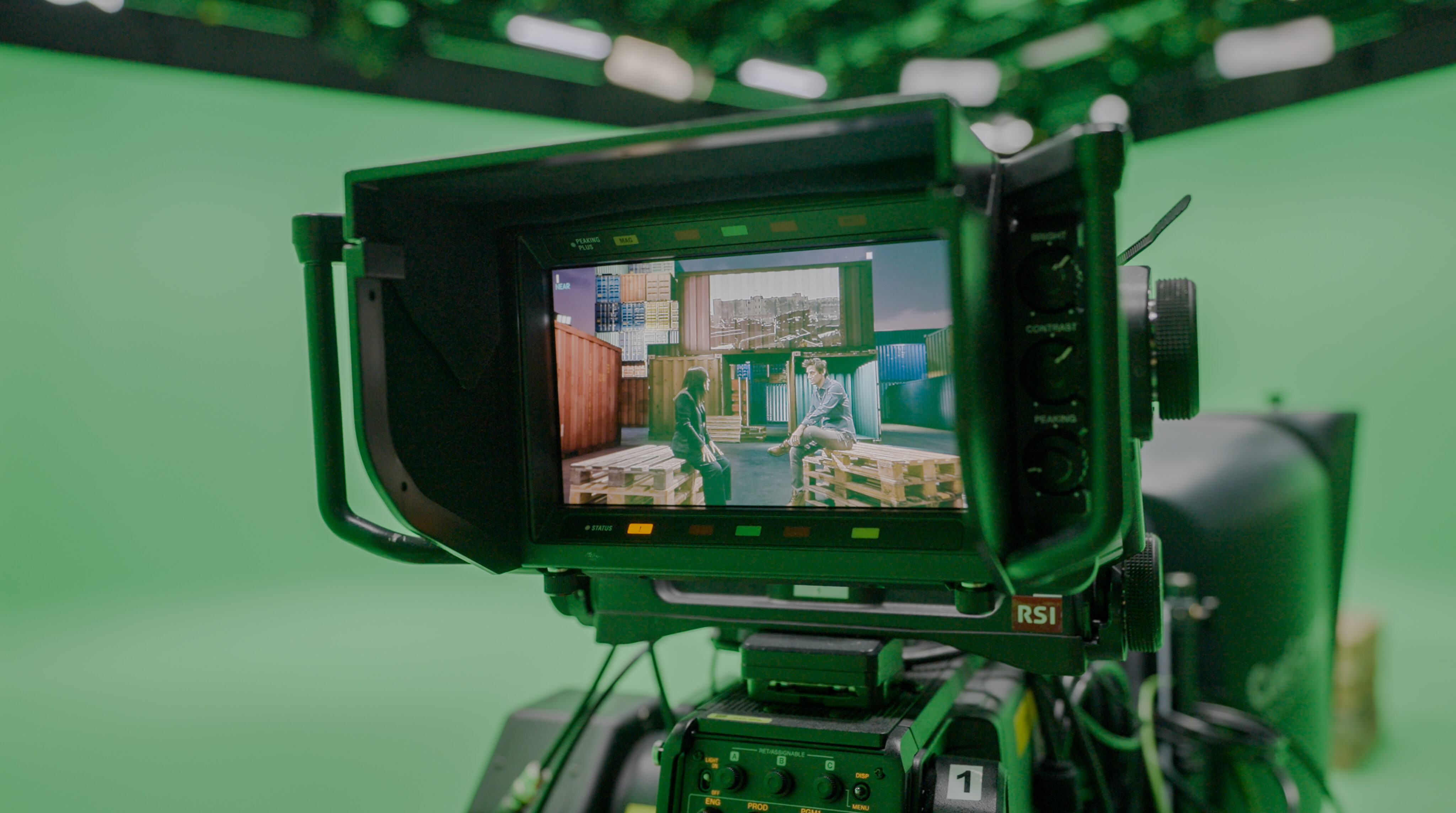 Live interview production viewed through a camera monitor, showing presenters seated in a green screen studio with virtual graphics and background elements composited live on-air.