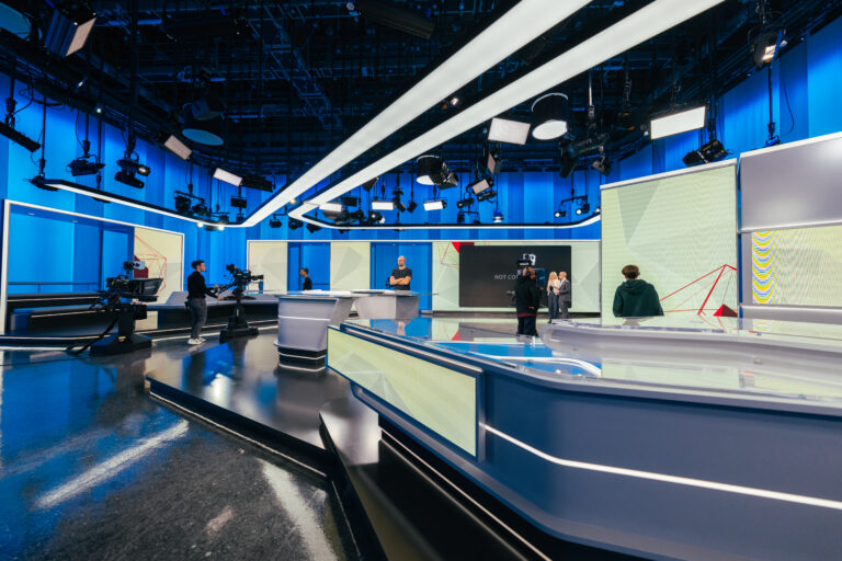 Wide shot of the RSI news studio during a live broadcast with production crew and presenters working on set.